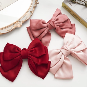 Three elegant satin bow hair clips in wine red, lotus pink and light pink on a desk
