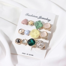 Close-up of three stylish hair clips with colorful gemstones and pearls on white fabric