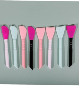 Multiple dual-ended silicone face mask brushes in pink and blue on a grey surface