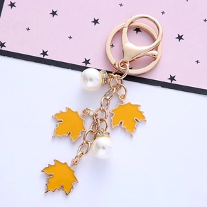 Detail shot of golden maple leaf keychain with elegant white pearls on a pink card