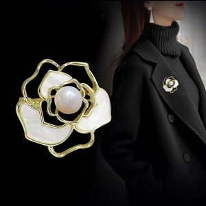 Detail of camellia brooch with white petals, gold trim and pearl on black background