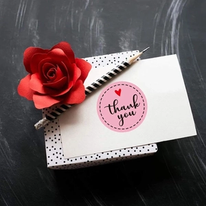 Macro shot of pink round 'thank you' stickers with red heart on gift box with roses