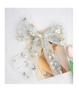 Detail of white gauze hair bow with pink flower embroidery and green leaf patterns