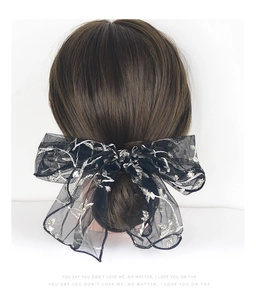 Detail of black lace bow hair clip with silver floral embroidery on a model's head