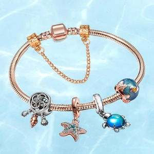 Rose gold ocean charm bracelet featuring sea turtle and starfish pendants on blue water background