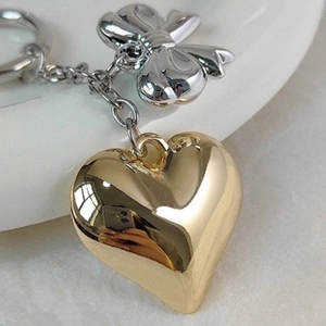 Golden heart and silver bow metal keychain charm for bags and headphones on white background
