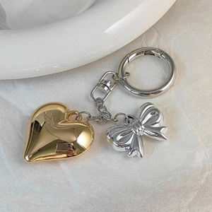 Metallic heart and bow keychain pendant on a white ceramic bowl and marble surface