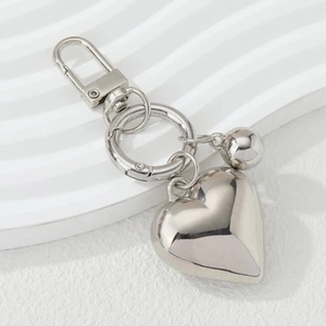 Silver hollow heart keychain with mini bell and lobster clasp on white wavy surface