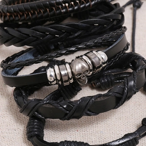 Macro detail of braided black leather bracelet set featuring silver skull and metal rings