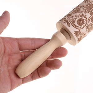 Macro shot of hand holding embossed wooden rolling pin with floral and geometric patterns