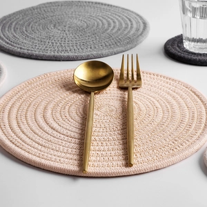 Pink hand-woven cotton heat-resistant round placemat with golden cutlery on top