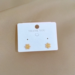 Minimalist gold snowflake stud earrings made of titanium steel on a white card display