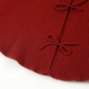 Large red knitted Christmas tree skirt with bow tie design and detailed cable stitch pattern