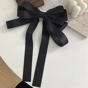 Elegant large black satin French bow hair clip with long ribbons on a white surface