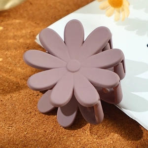 Detailansicht der mattvioletten Gänseblümchen-Haarklammer auf weichem Korkhintergrund