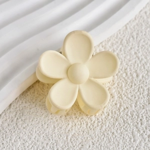 Detailed top view of a matte yellow flower-shaped hair claw clip on a textured surface
