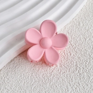 Detail shot of a matte light pink flower hair claw clip on a textured white background