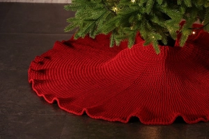 Detailed knit texture of large red Christmas tree skirt with ruffled edges and wool yarn
