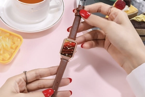 Elegant woman wearing square rose gold watch with brown leather strap in a cafe setting