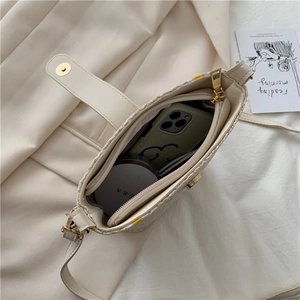 Minimalist beige woven bucket bag with leather flap and metallic magnetic closure