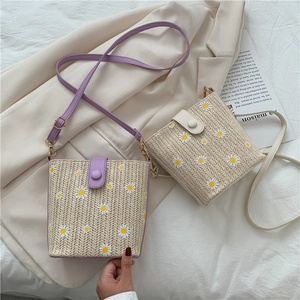 Detail of straw bucket bag with daisy embroidery in purple and white colors