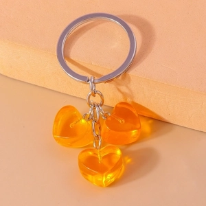 Close-up of three amber resin heart charms on a silver keychain over an orange surface