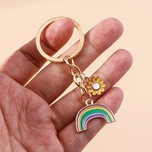 Rainbow and daisy floral keychain with golden metal clasp held against pink background