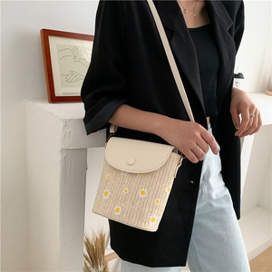 Detail of woven straw bucket bag featuring white daisy prints and a cream PU leather strap