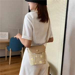 Chic straw woven bucket bag with daisy accents and khaki flap worn by a model