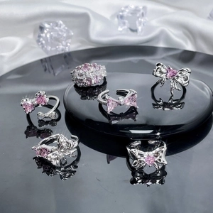 Silver bow rings with pink zircon gems set on black reflective surface with silk