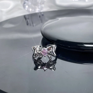 Detail of silver bow ring with pink square zircon on reflective black surface