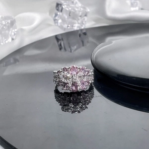 Close-up of silver ring featuring pink oval gemstones and bow design on black reflective surface