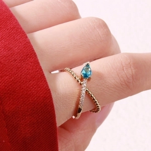 Detailed view of a gold wheat-wave ring with blue teardrop stone and pavé diamonds