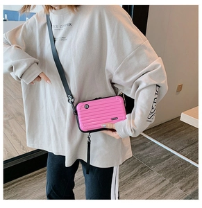 Mini pink hard shell suitcase crossbody bag with adjustable strap worn by model