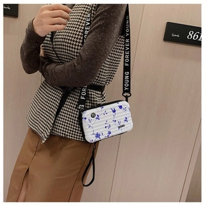 Close-up of white mini suitcase bag with blue rose pattern and wide branded strap