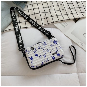 Detail of a white hard-shell mini suitcase bag with blue floral patterns and wide strap