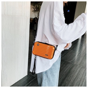 Detail view of orange hardshell mini suitcase crossbody bag with logo strap and logo