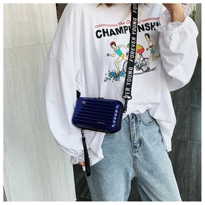 Close-up of royal blue mini suitcase crossbody bag with logo strap on white outfit