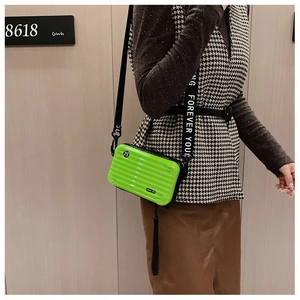 Detail of a bright green mini suitcase crossbody bag with Forever Young strap and metal logo