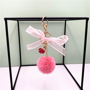 Close-up of pink fluffy pompom keychain with lace bow and tassel on a geometric stand