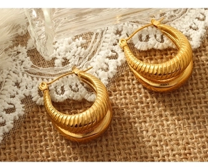 Detailed view of gold plated U-shaped twisted hoop earrings on white lace background