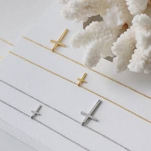 Collane minimaliste con croce in oro e argento su supporto bianco testurizzato