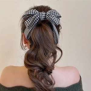 Detail of a chic black and white houndstooth bow hair clip on a ponytail