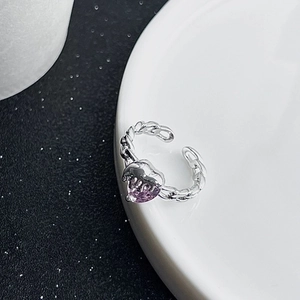 Close-up of heart-shaped purple zircon ring with silver chain band on a ceramic plate