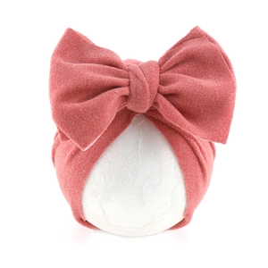 Detail of soft cashmere-like pink baby turban hat with oversized bow on lace display