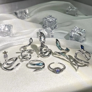 Silver snake rings set with blue gemstones on white silk background with ice cubes