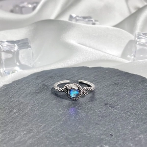 Detail of snake shaped silver ring with blue gemstone on slate and white silk background