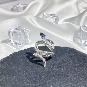 Macro shot of silver snake ring with blue pear gemstone and crystals on dark stone