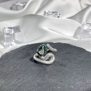 Detail of silver snake ring with green enamel and clear gemstone on dark stone base