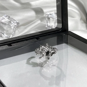 Detailed view of a silver butterfly ring with dark gemstone on white silk and ice props